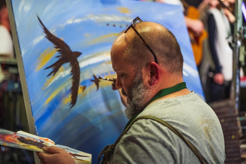 Chris Duffett painting at Fresh Streams conference, his canvas features birds in the sky