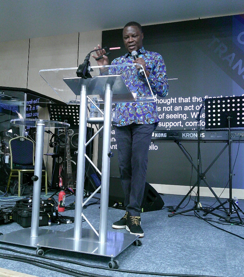 Osoba Otaigbe standing at a lecturn, speaking into a microphone 