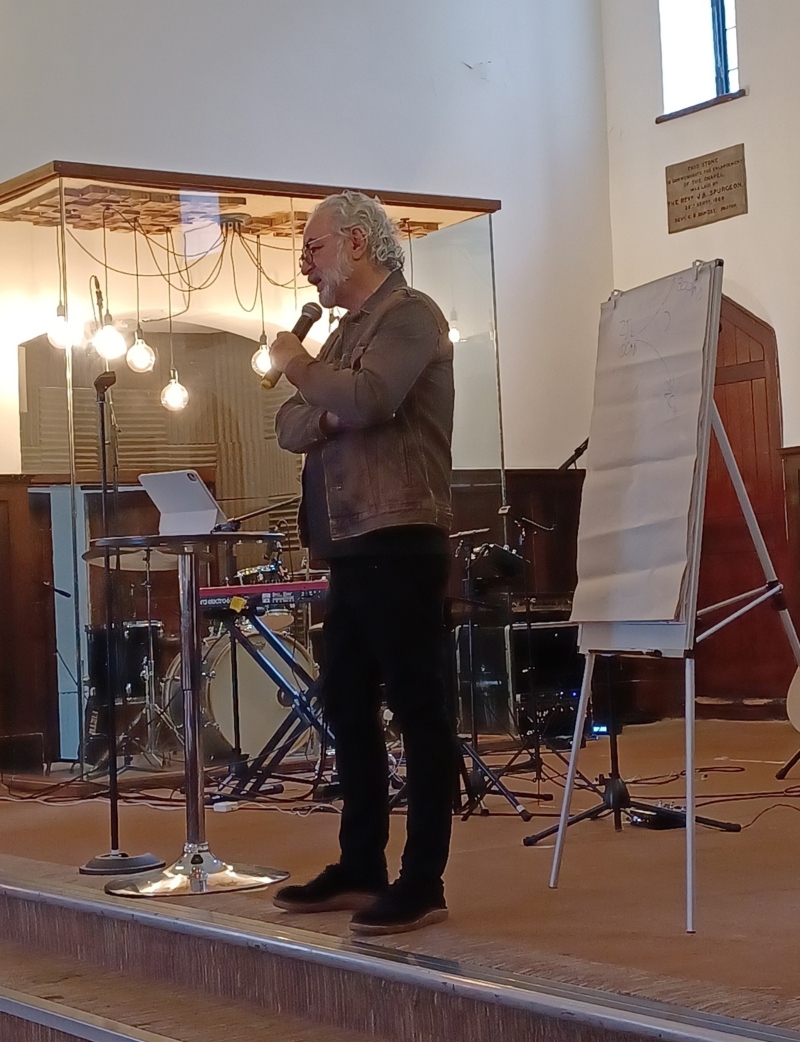Alan Hirsch holding a microphone and speaking on stage at the Everyone Everywhere conference