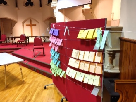 A red screen in a church displays colourful sticky notes arranged in a creative pattern.
