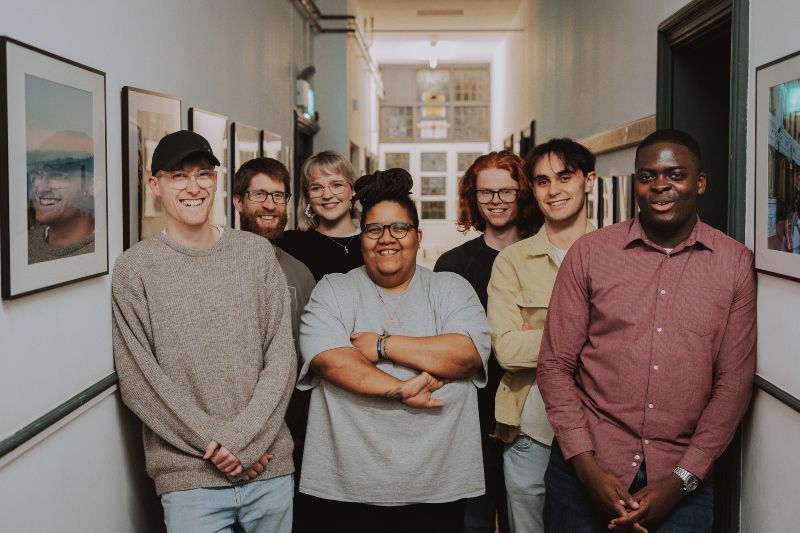 Seven members of The Well Collective smile for the camera in a corridor at the back of the church