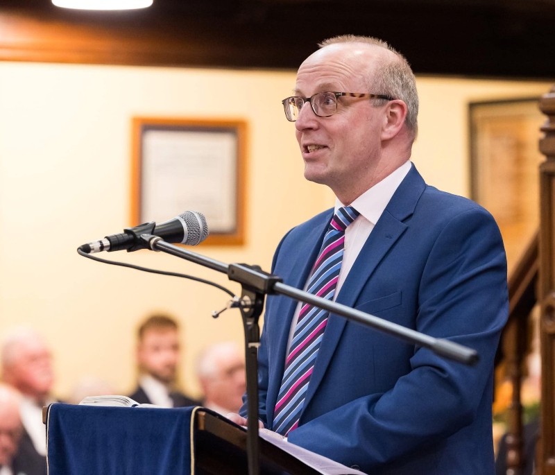 Rob May in a suit and tie speaking at a podium
