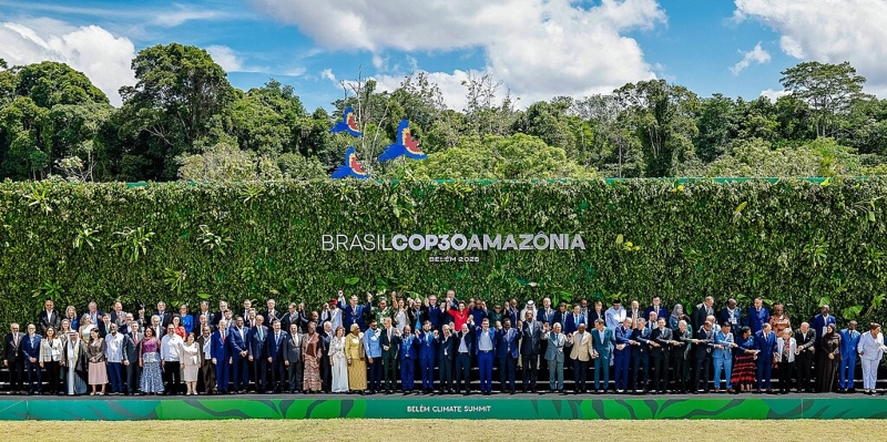 Brasil COP30 - official photograph - a diverse group of people stands together in front of a vibrant green wall that contains the COP30 sign