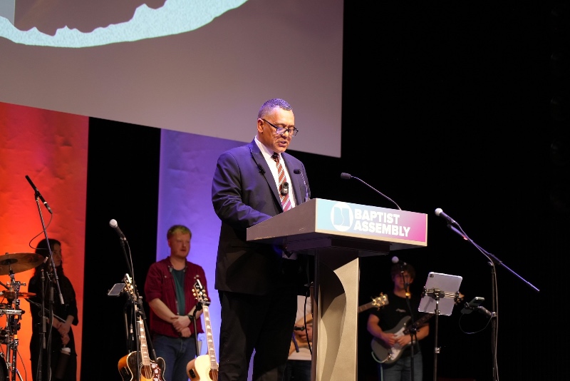Alex Afriyie preaching at a podium at the 2026 Baptist Assembly