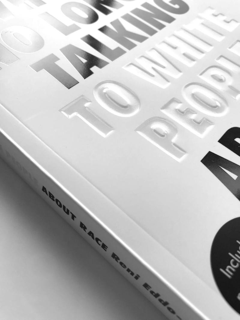 A close-up, black-and-white angled view of the book cover and spine for "Why I'm No Longer Talking to White People About Race" by Reni Eddo-Lodge, showing embossed lettering on the white cover.
